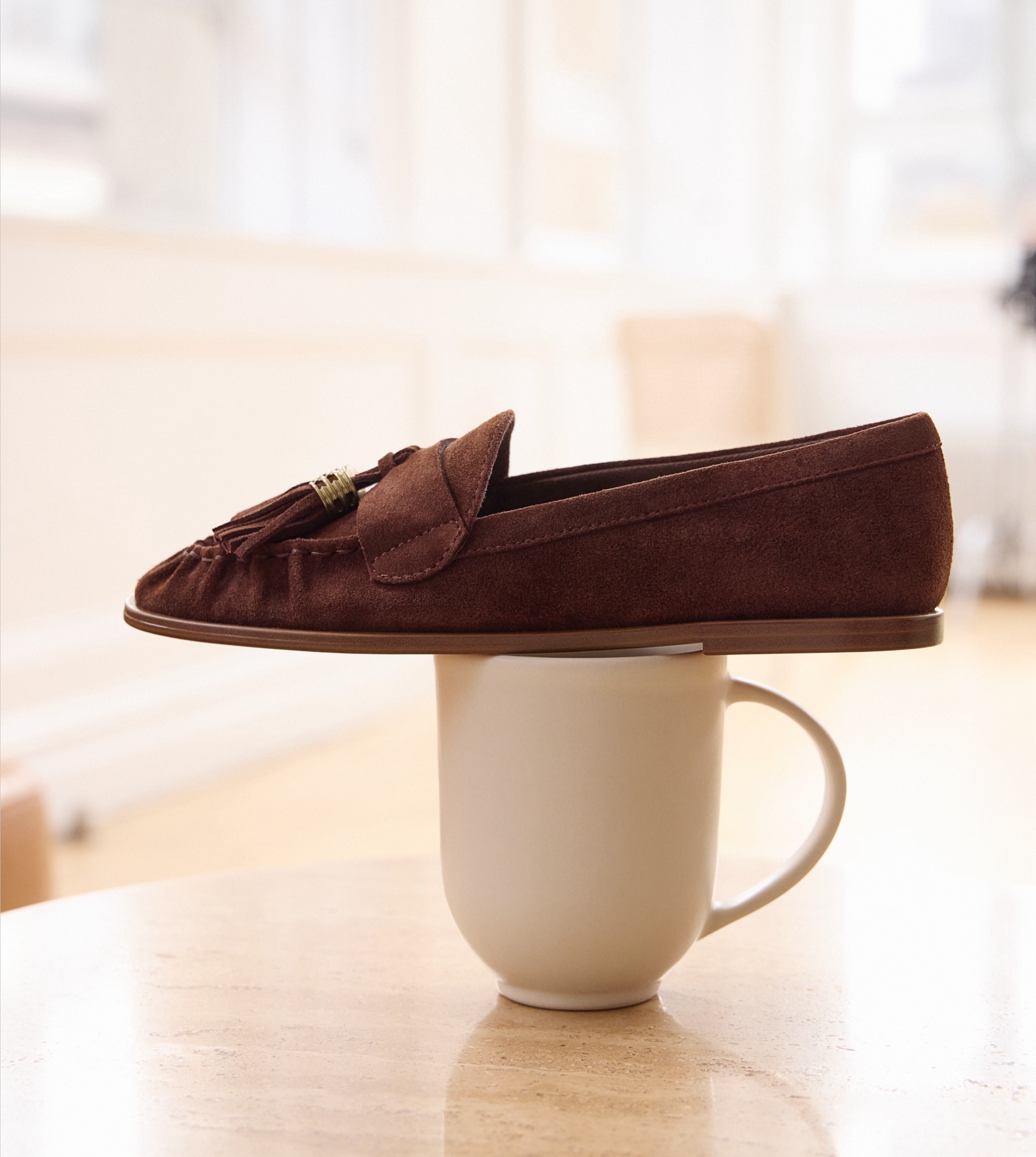 the hartley tassel loafer in hickory brown sitting on top of a coffee mug