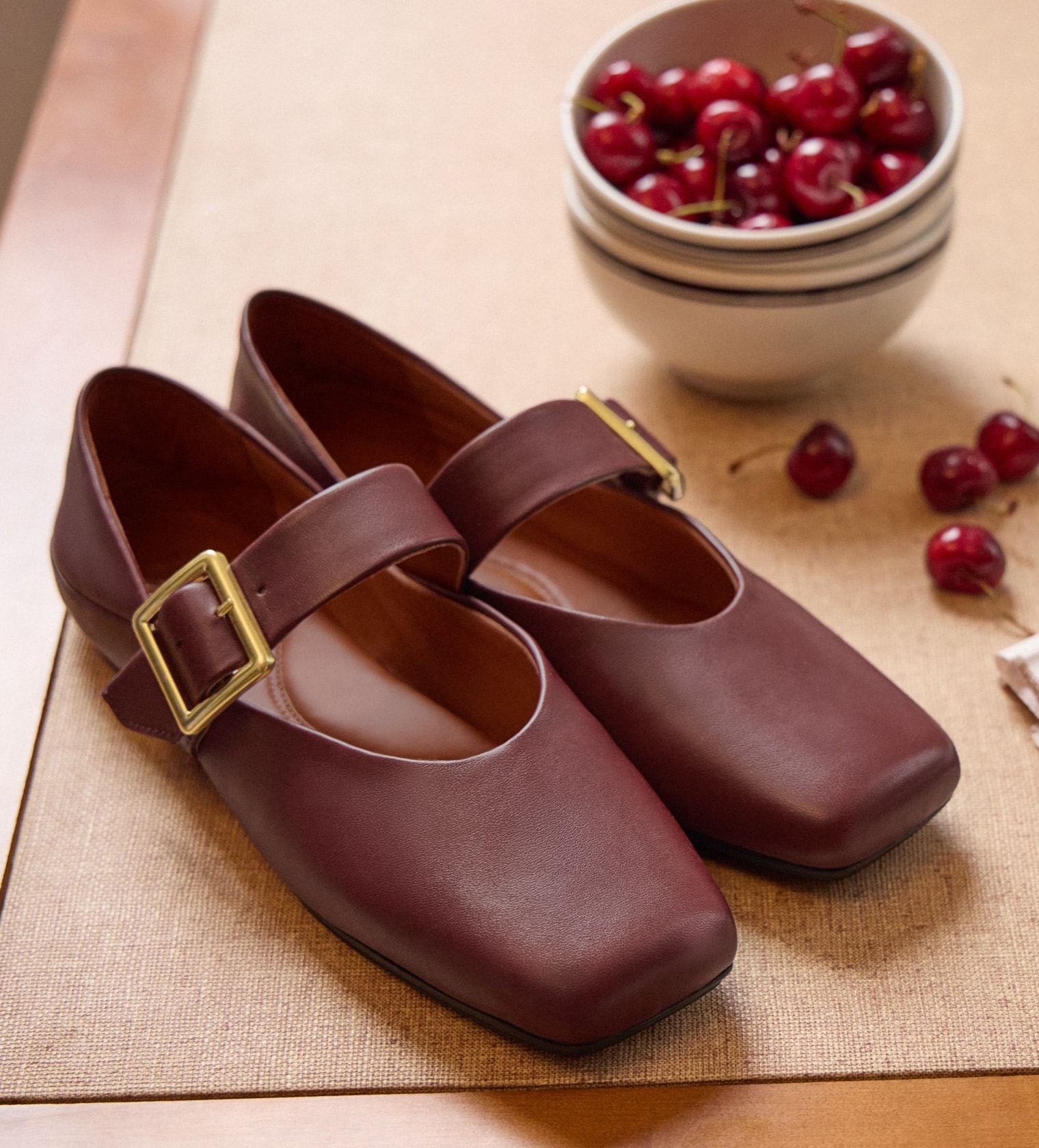 the oakes mary jane flat in burgundy sitting next to a bowl of cherries