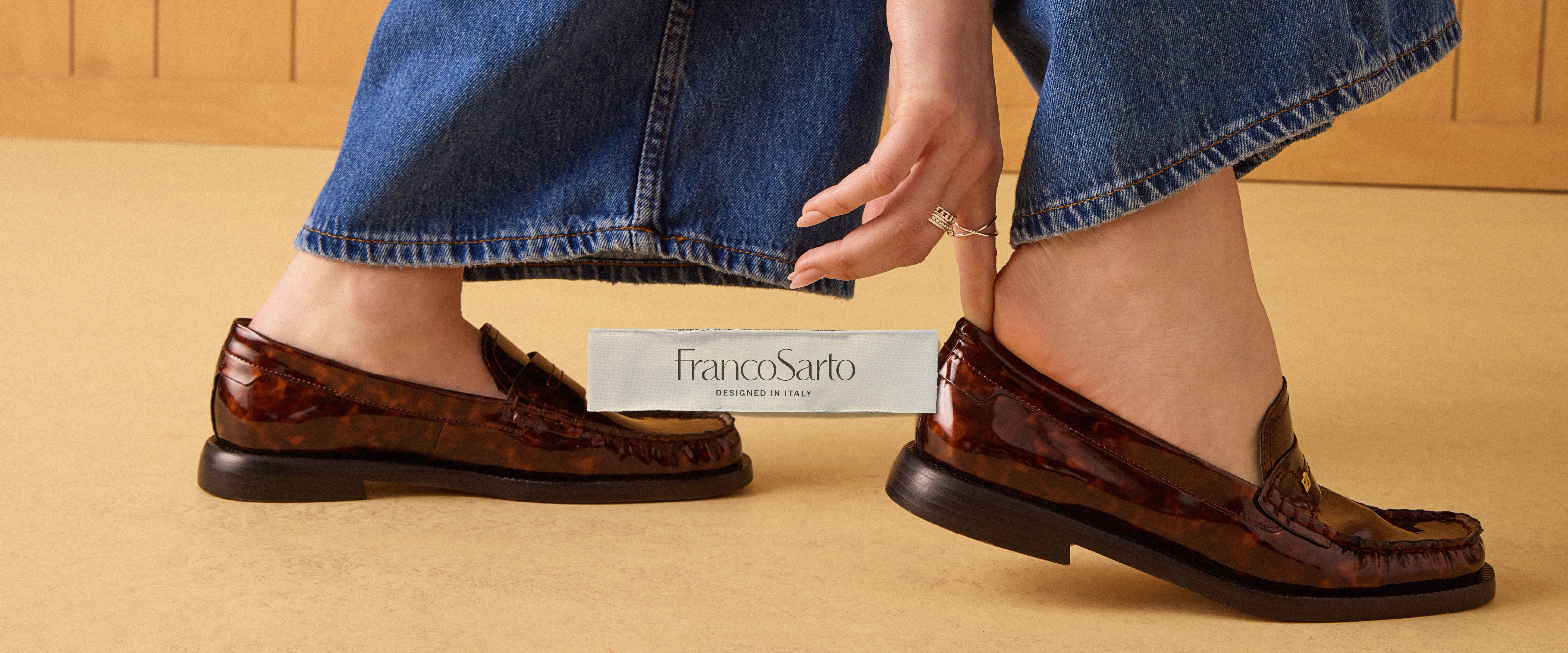 A woman slipping on a pair of tortoise-print patent leather loafers. The Franco Sarto logo is overlaid.