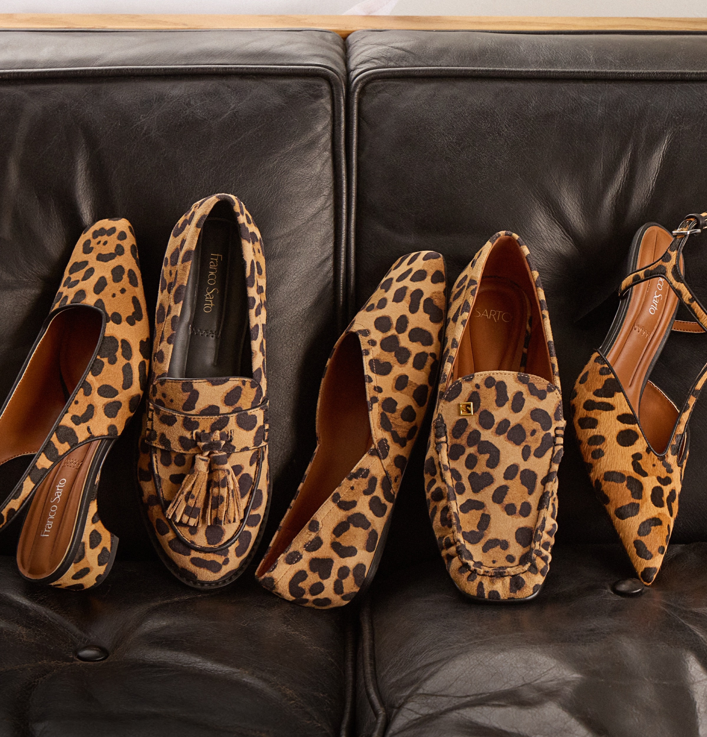 Various types of women’s leopard shoes displayed on a brown leather couch. 