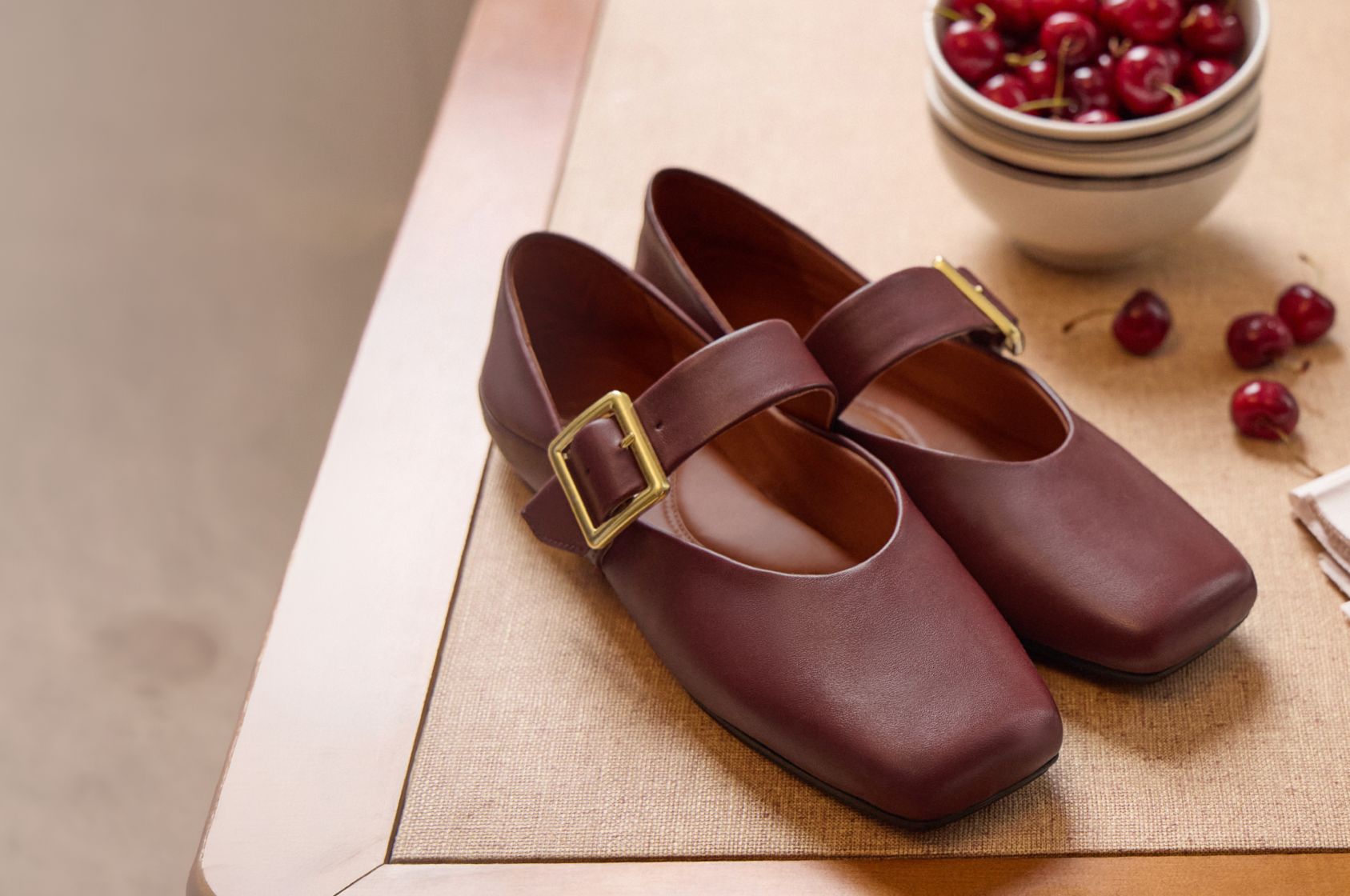 Franco Oakes Mary Jane in Bordo red leather, single strap with gold buckle, styled on a table with a bowl of cherries.