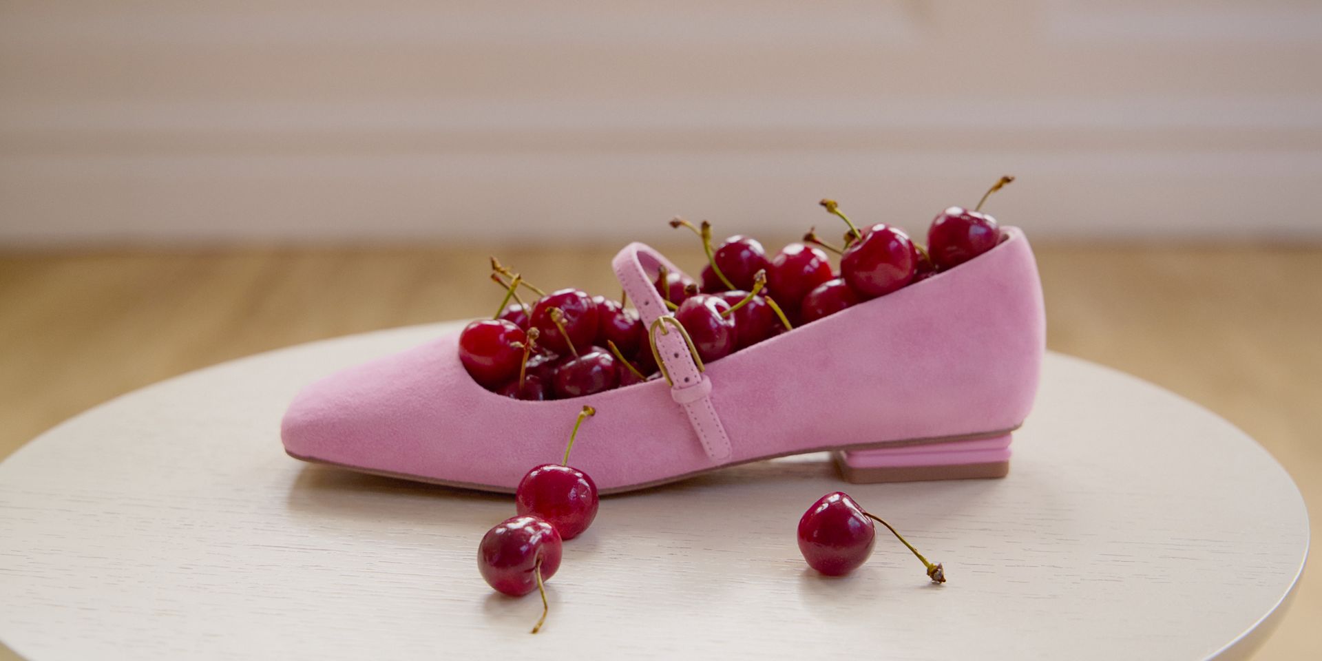 Tinsley Mary Jane flat in pink suede,  styled on a white surface and filled with cherries. 