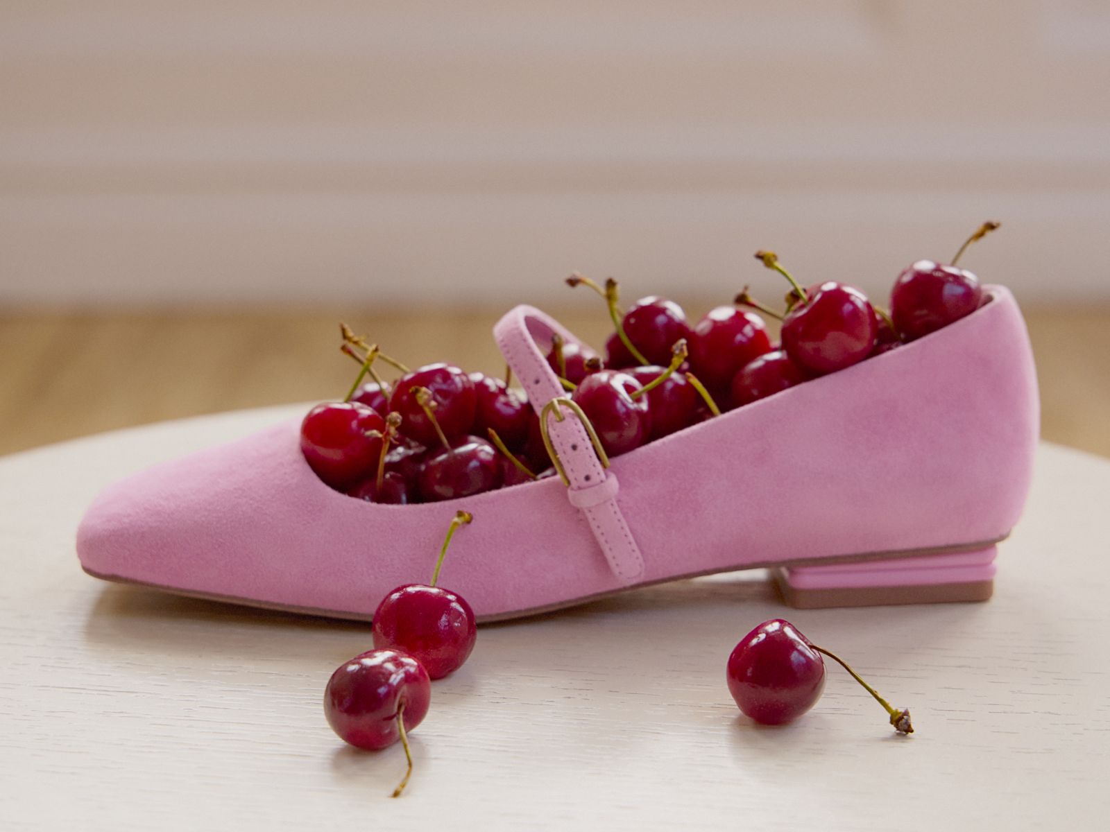 Tinsley Mary Jane flat in pink suede,  styled on a white surface and filled with cherries. 