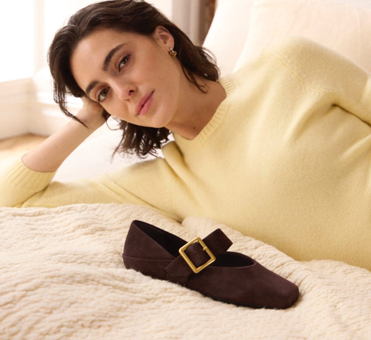 woman in a pastel yellow sweater lying down with the oakes mary jane flat in suede brown