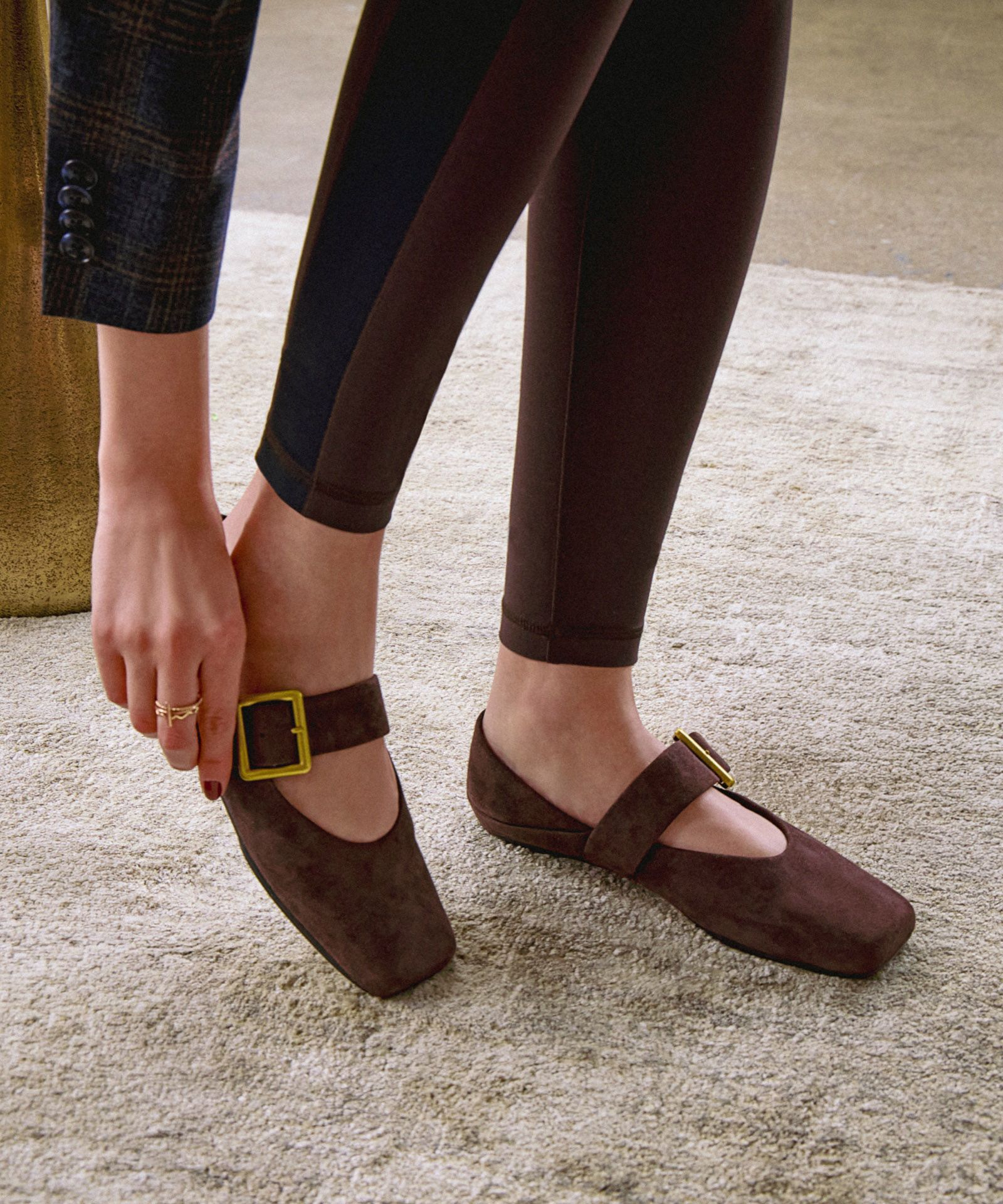 Person adjusting the strap on a brown suede Franco Sarto Oakes Mary Jane with a gold buckle.